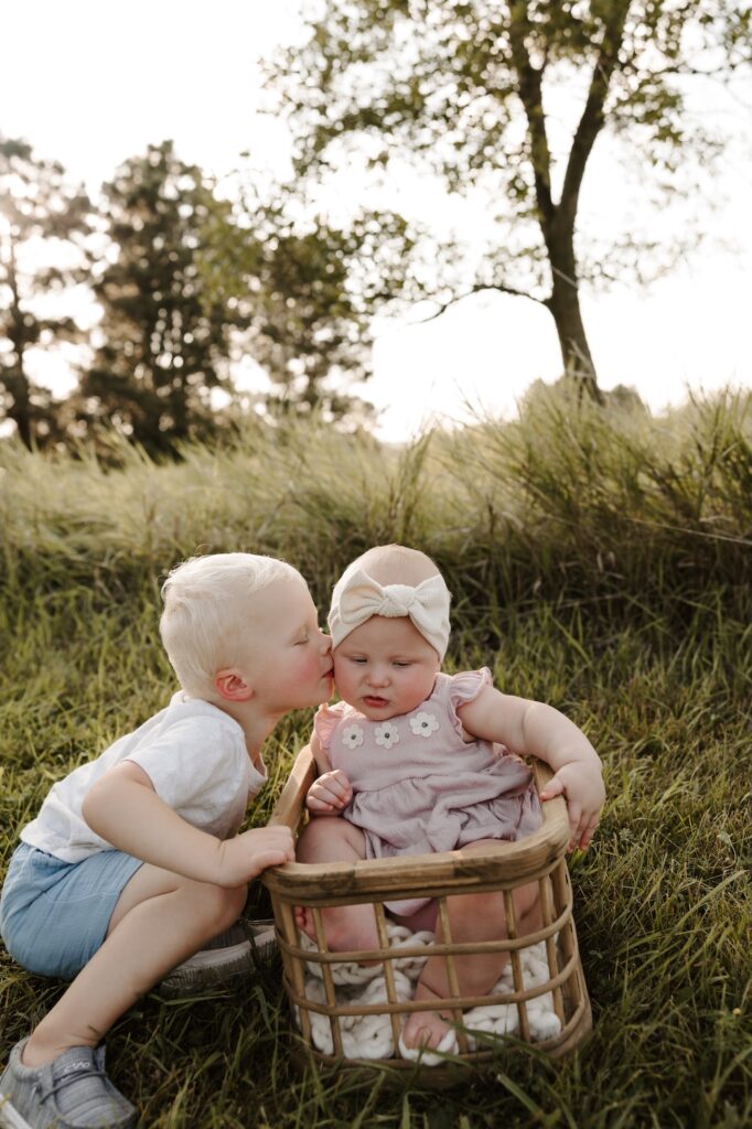 a photo of a brother kissing his sister as she is sitting in a basket