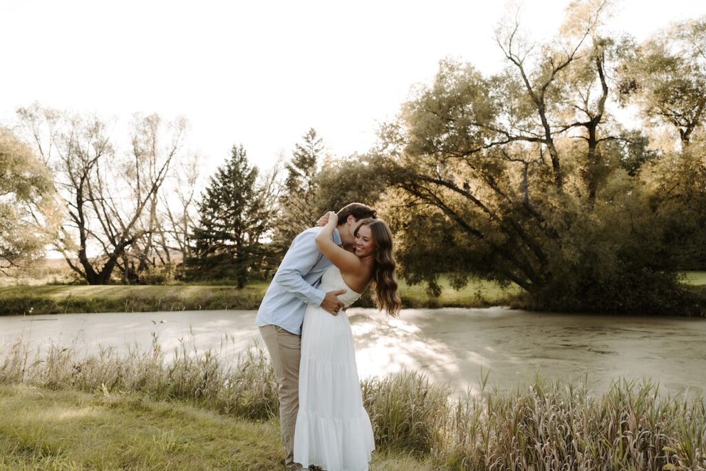 guy dipping girl back to give her a kiss on the neck with a beautiful lake behind them