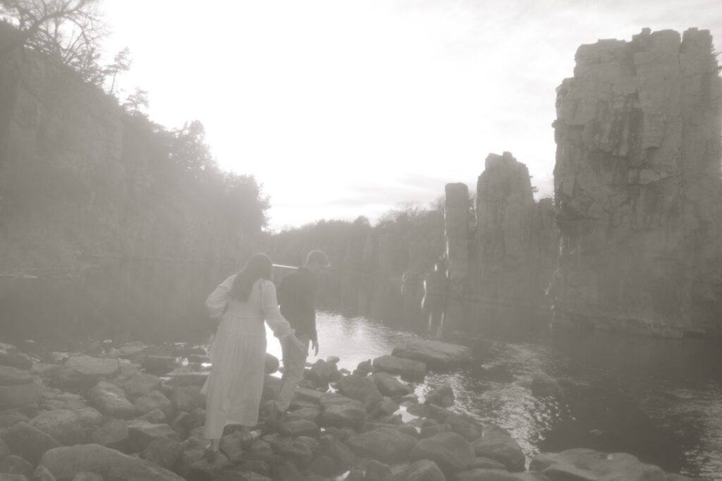 male leading a female while walking on rocks while a photographer takes their photo