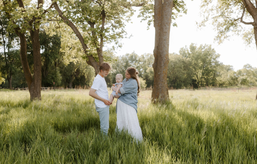 a family of 3 standing in a field while a photographer takes their photo